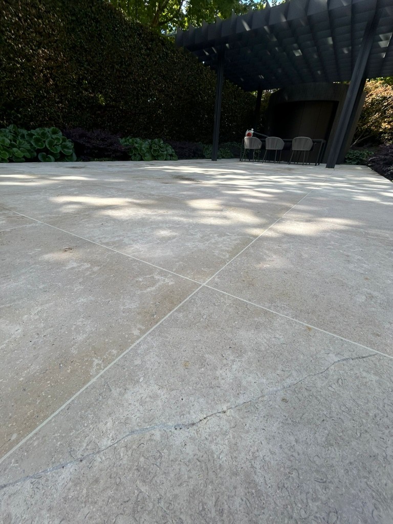 Honed limestone tile patio under a pergola in landscaped garden