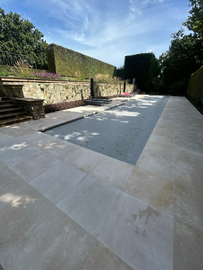 Limestone-tiled pool deck with stone retaining wall and garden