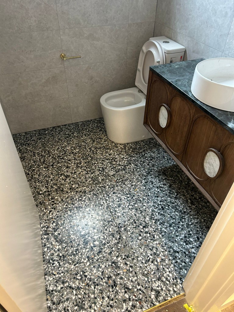 Black and grey terrazzo bathroom floor with densely packed marble chips and timber vanity
