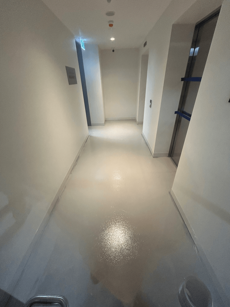 Cream metallic epoxy floor in long Melbourne commercial corridor with white walls